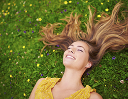 A woman lying in the grass outside, basking in the sunshine.