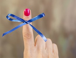 An index finger with sparkly pink nail polish and a blue ribbon tied around it.