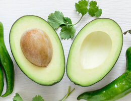 Two halves of an avocado, with green peppers and cilantro.