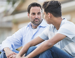 A man and a teen sit outside a home.