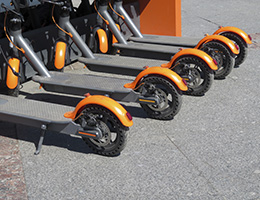Five orange and black electric scooters sit in a row. 